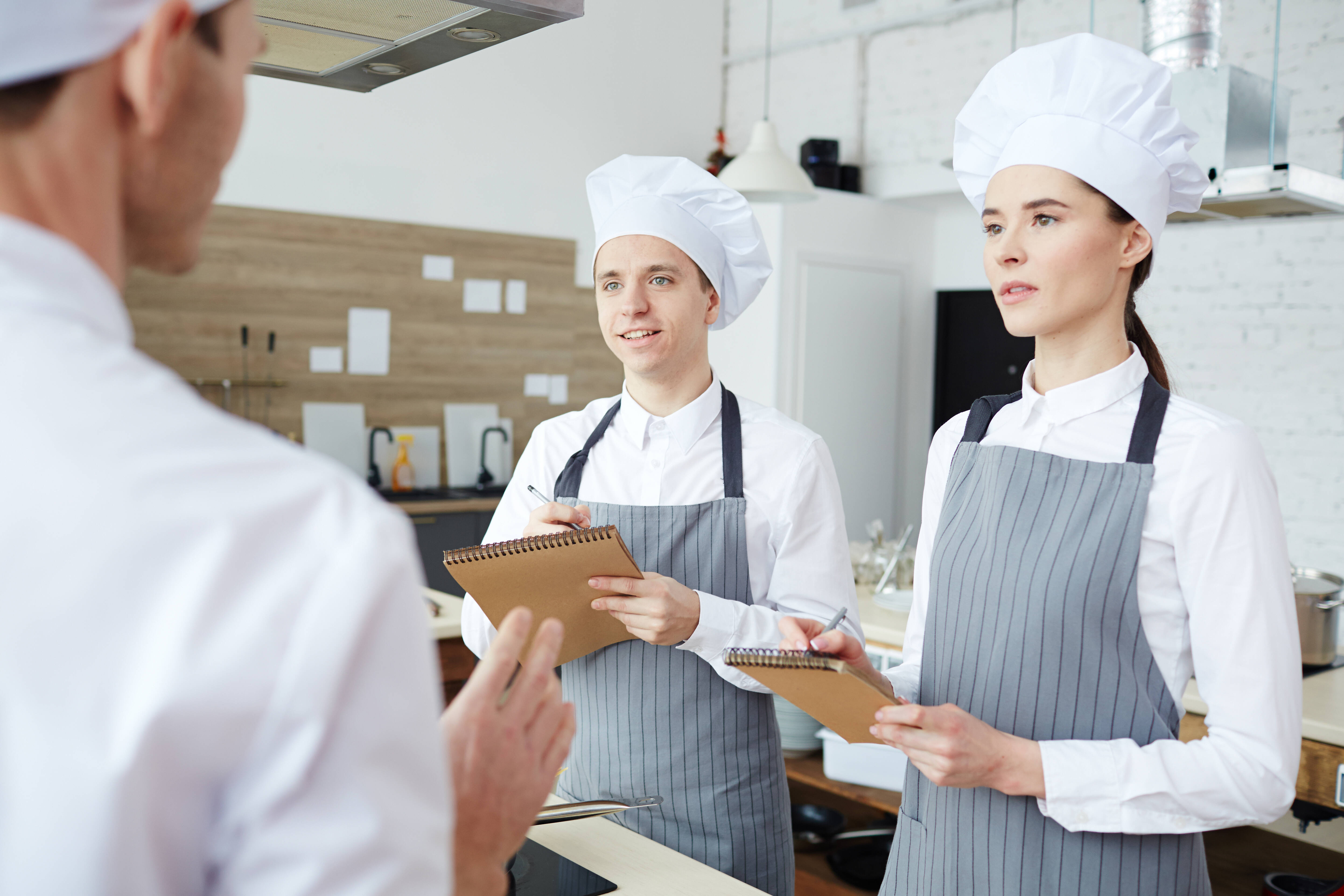 Two young chef trainees listening to advice about cooking while working in the kitchen